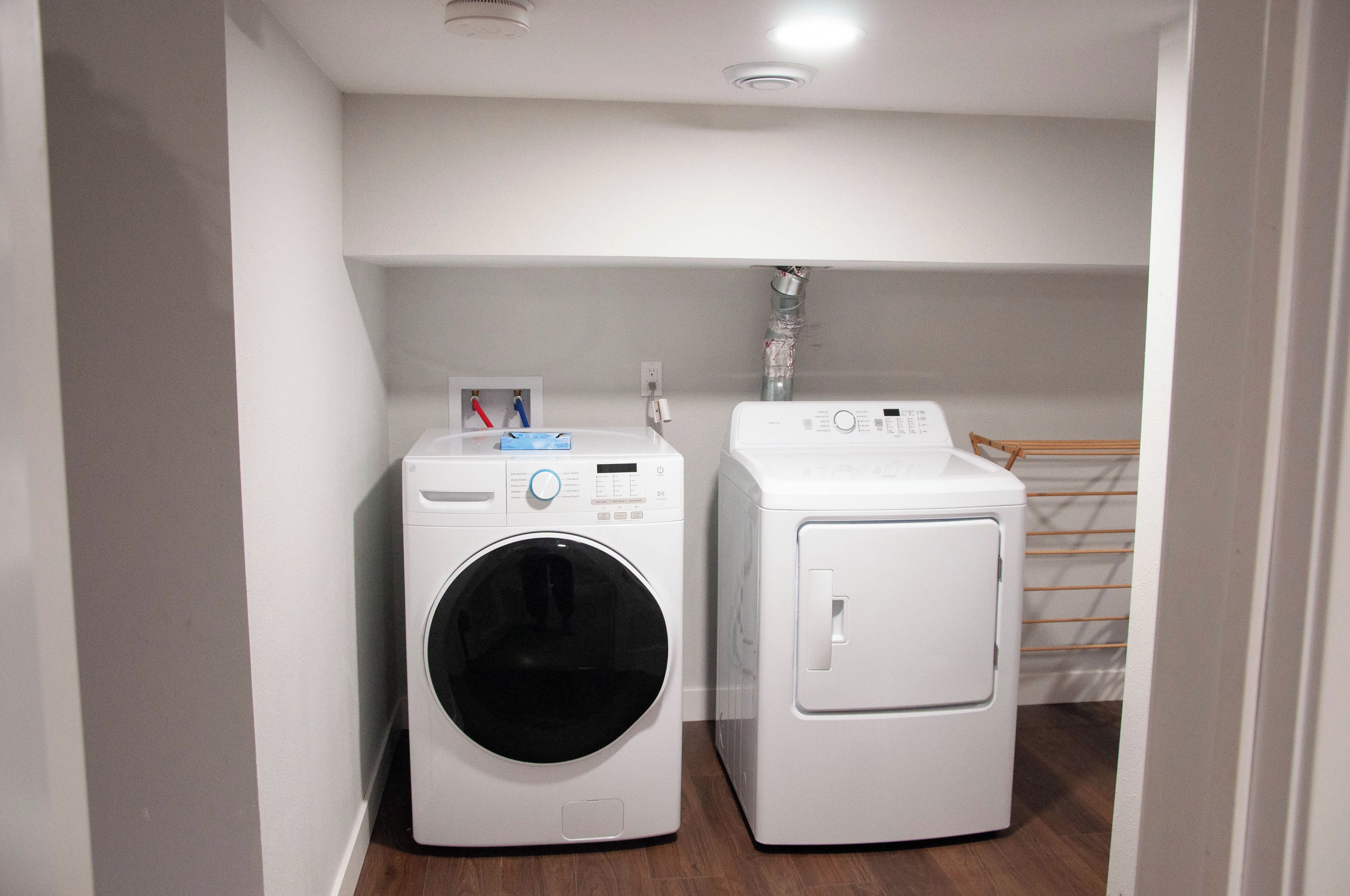 A laundry room with two white washing machines and a drying rack.