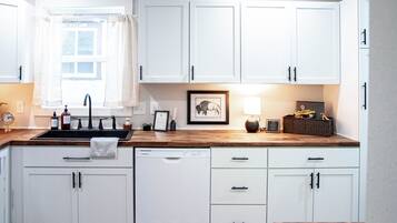 A kitchen with white cabinets, a wooden countertop, a dishwasher, and a window with curtains.