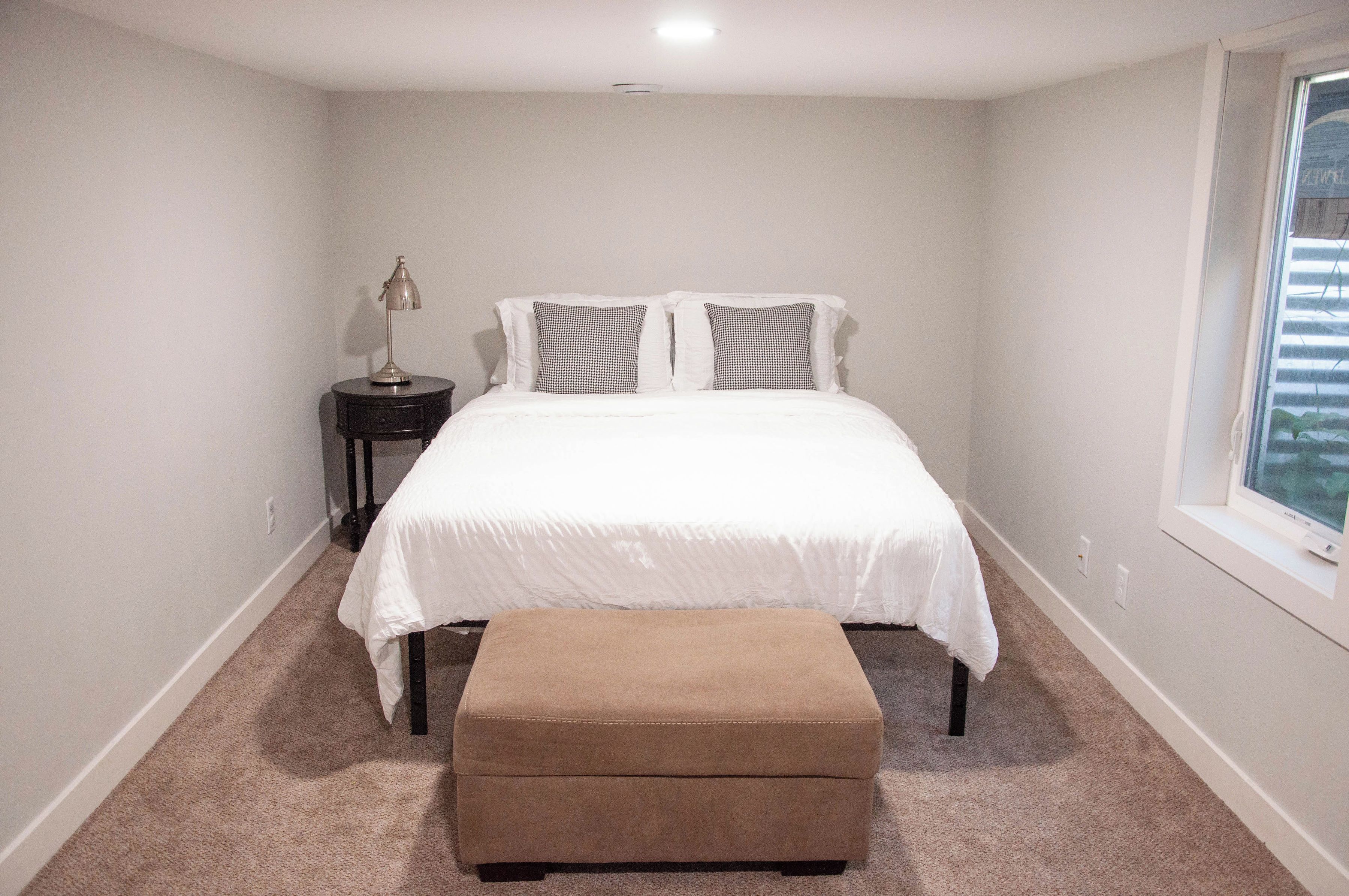 Une chambre à coucher avec un lit, une table de chevet, une lampe et une fenêtre.