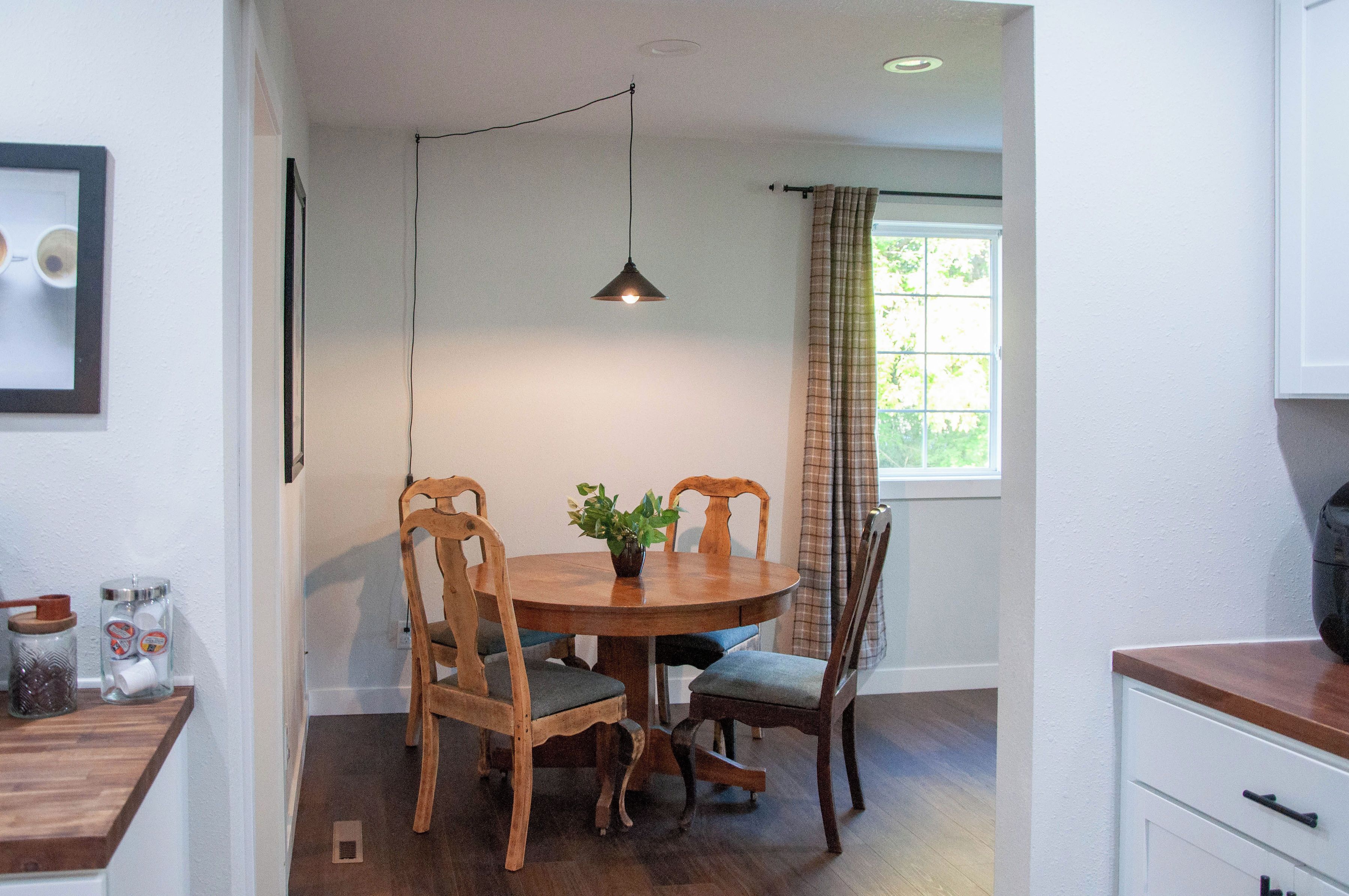 A dining area with a round table, two chairs, a hanging pendant light, and a window with curtains.