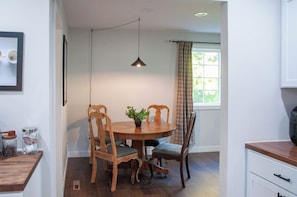 Un coin repas comprenant une table ronde, deux chaises, un luminaire suspendu et une fenêtre avec des rideaux.