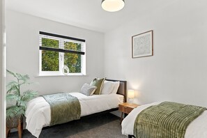 A bedroom with two single beds, a window with blinds, a bedside table with a lamp, and a framed picture on the wall. - Cambridge home with parking & garden (Cambridge)