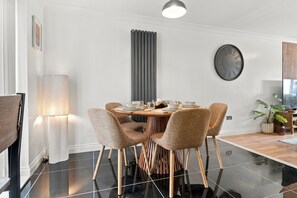 A modern dining area with a round table, six chairs, a wall clock, and a vertical radiator. - Cambridge home with parking & garden (Cambridge)