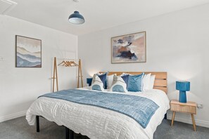 Un dormitorio con una cama, una mesita de noche, una lámpara y dos cuadros en la pared.