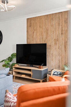 Una sala de estar moderna con un televisor de pantalla plana sobre un soporte de madera, un sofá gris y un sillón naranja.