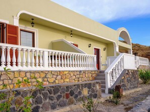 A building with a stone facade, white railings, and a red door. - One Bedroom Villa with Sea View, Kaminia Holiday Homes (Thira - Santorini)