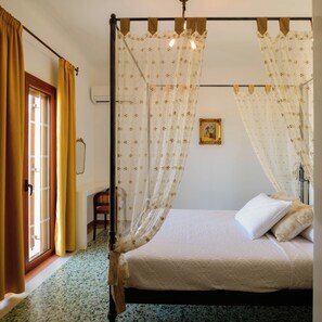 A four-poster bed with a canopy, a chair, a picture frame on the wall, and a door with curtains. - One Bedroom Villa with Sea View, Kaminia Holiday Homes (Thira - Santorini)