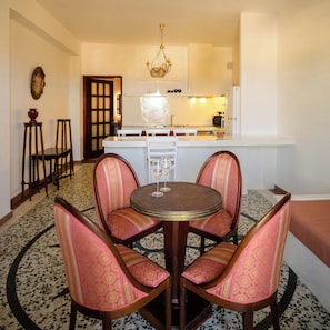 A dining area with a round table and four chairs, a kitchen in the background, and a patterned floor. - One Bedroom Villa with Sea View, Kaminia Holiday Homes (Thira - Santorini)