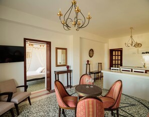 A hotel room with a bed, a dining area with a table and chairs, a kitchen area, and a chandelier. - One Bedroom Villa with Sea View, Kaminia Holiday Homes (Thira - Santorini)