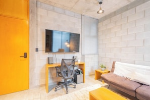 Una sala de estar moderna con una pared de ladrillo, un televisor sobre un escritorio, un sofá marrón y una pequeña mesita con una planta.