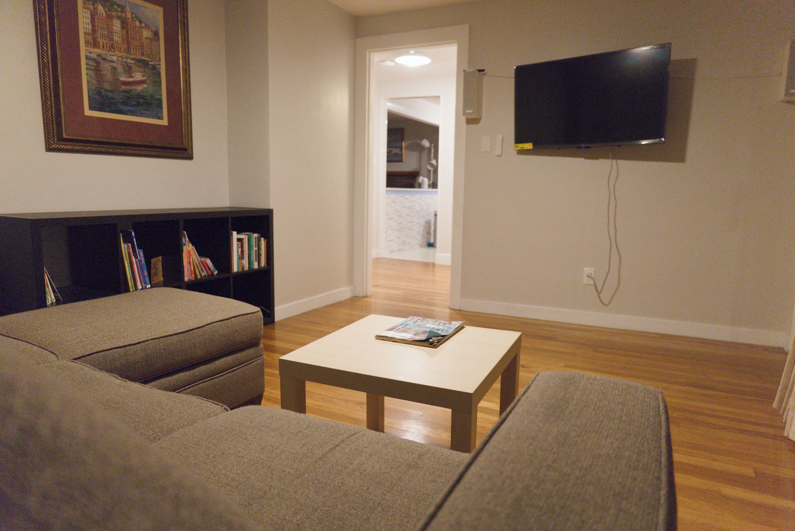 A living room with a sofa, a coffee table, a bookshelf, and a TV mounted on the wall.