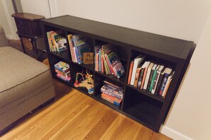 A bookshelf with various books and games, a small wooden table, and a grey upholstered bench. - Spacious 3-Bedroom House in Boston with Free Parking (Boston)