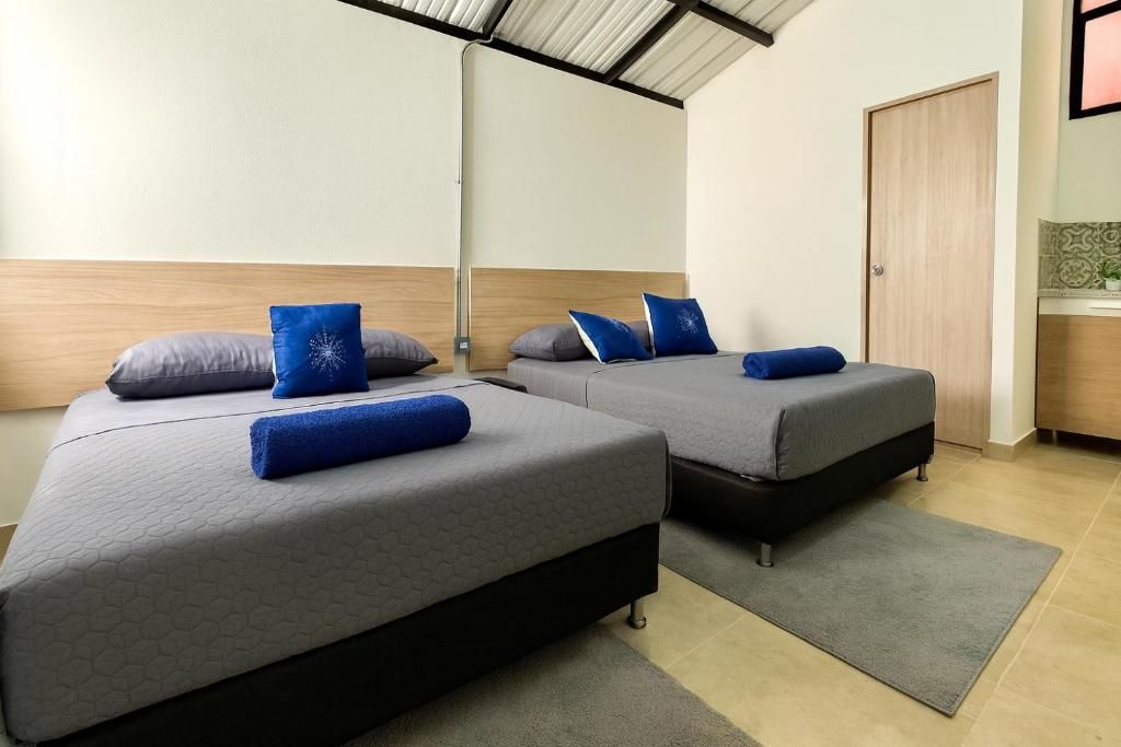 A hotel room with two beds, each with a grey mattress and blue pillows. There is a wooden headboard, a grey rug, and a wooden door.