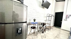 A kitchen with a stainless steel refrigerator, a small table with two chairs, and a wall-mounted TV. - Sinu Loft (Medellín)