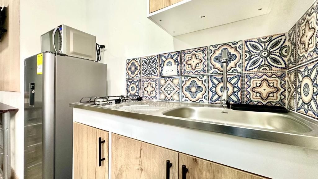 Cocina con refrigerador de acero inoxidable, lavamanos y azulejos decorativos en la pared.