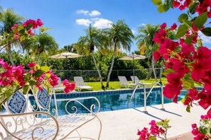 A poolside area with lounge chairs and umbrellas, surrounded by palm trees and bougainvillea flowers. - Villa Paradise PalmeraPrivate Pool Oasis (Port Charlotte)