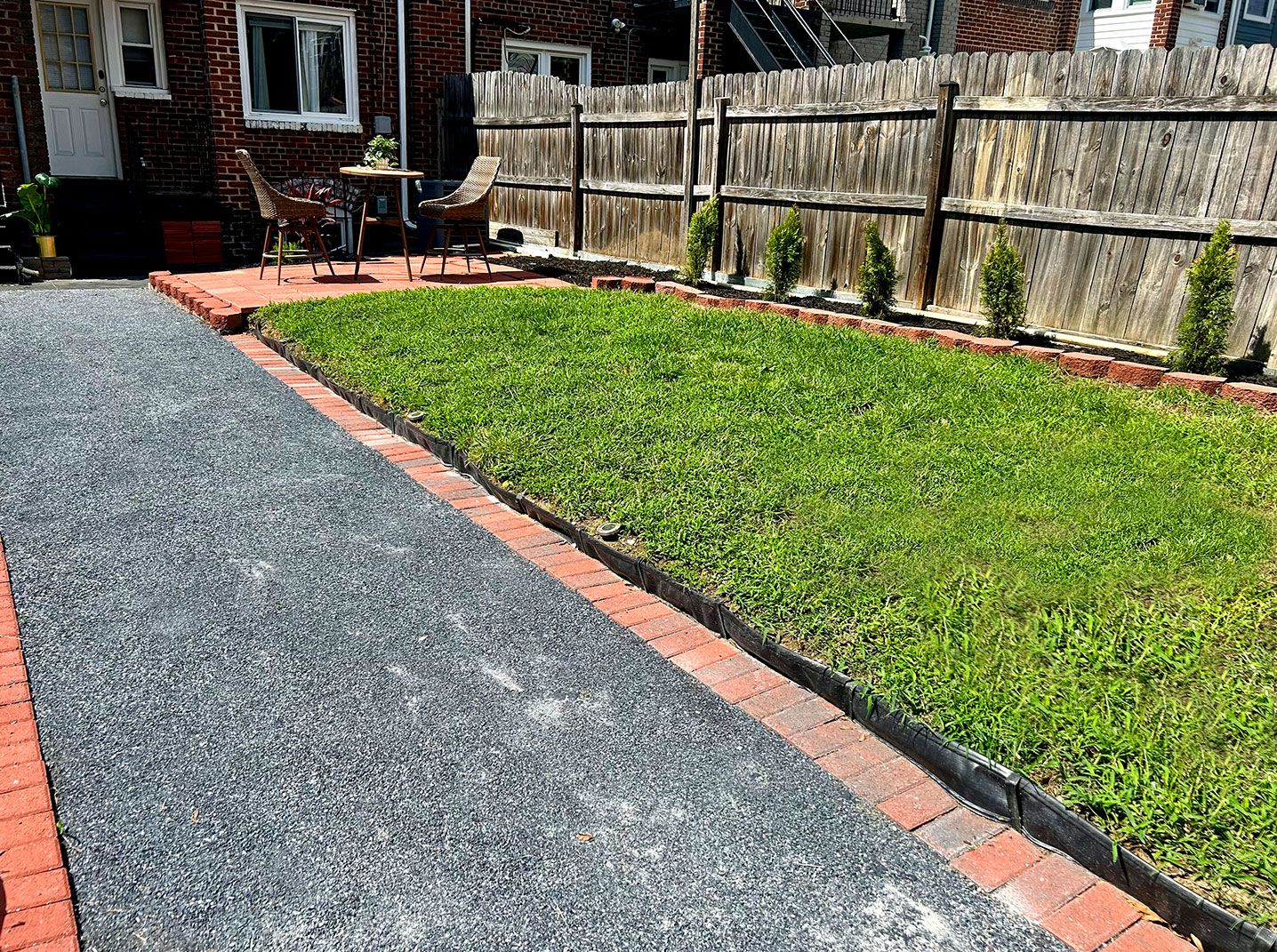 A residential street with a paved road, a grassy area with a brick border, and a wooden fence.