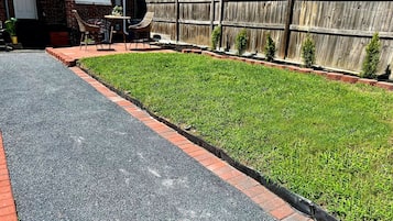 A residential street with a paved road, a grassy area with a brick border, and a wooden fence.