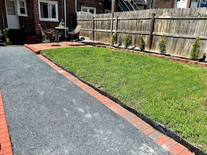 A residential street with a paved road, a grassy area with a brick border, and a wooden fence.