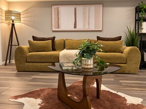 Un salon avec un canapé, une table basse en verre, une lampe et un tableau accroché au mur.