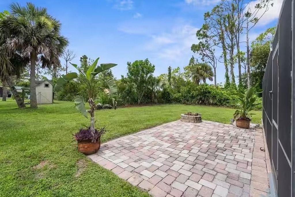 A paved patio area with a brick pattern, surrounded by a grassy lawn and various plants.