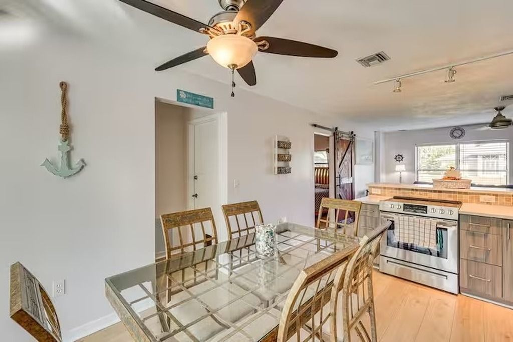 Zona pranzo con tavolo e sedie in vetro, ventilatore a soffitto e cucina con forno.