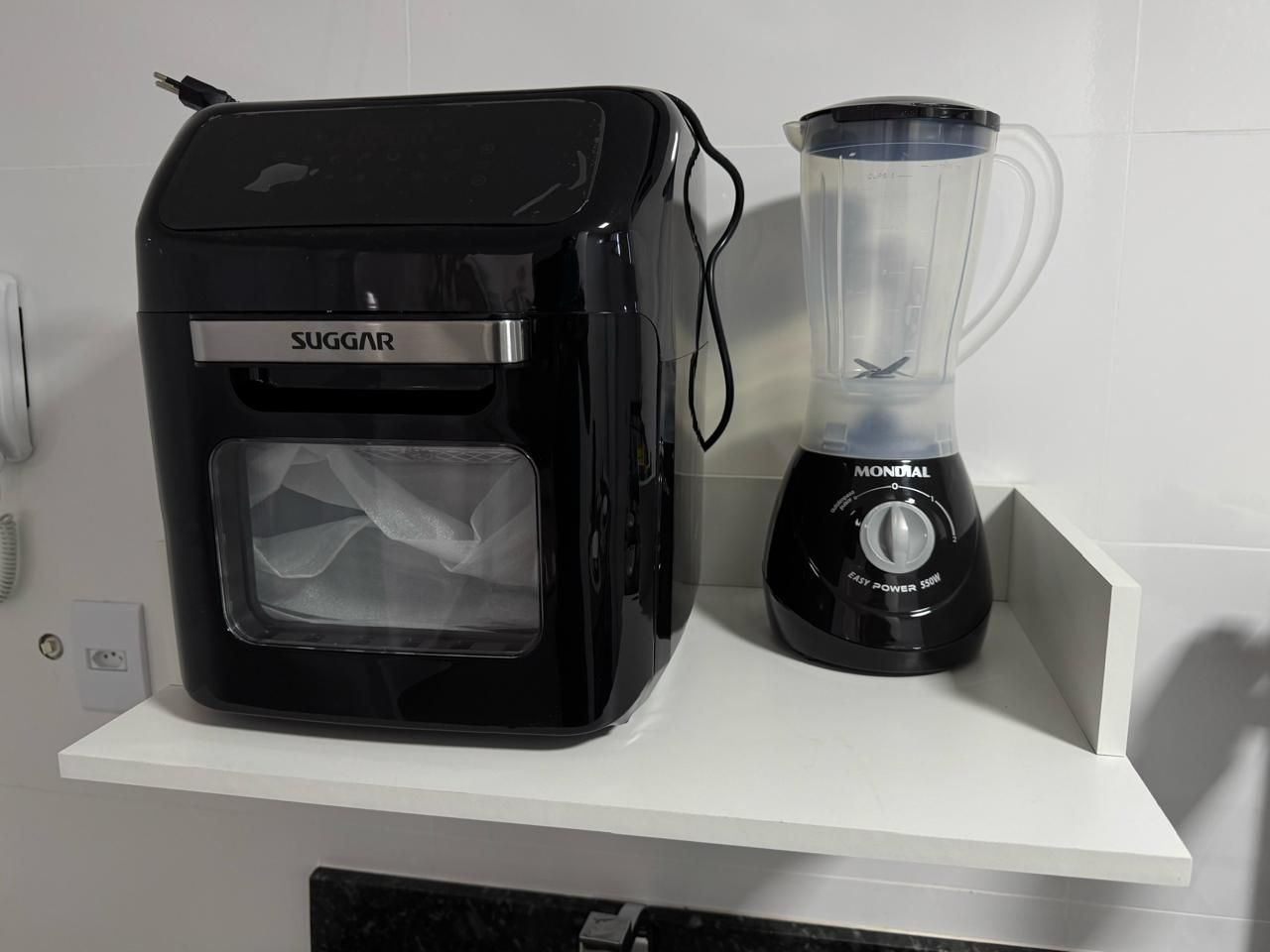 Una cucina con un bollitore elettrico nero e un frullatore su un piano di lavoro bianco.