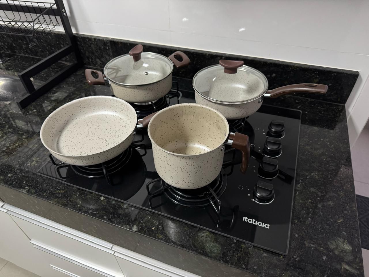 Cozinha com fogão preto, quatro panelas e coifa.