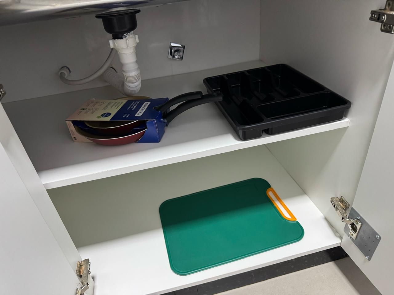 Una cucina con lavastoviglie integrata, un lavello e un piano di lavoro con tagliere e un vassoio nero.