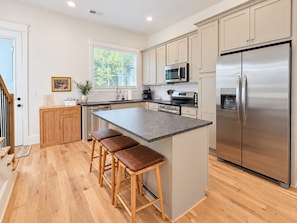 A modern kitchen with a central island, stainless steel appliances, and wooden flooring. - Homewood Luxury 2 Bedroom 2 Bath Townhome 3020 (Homewood)