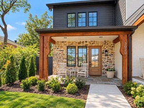 A two-story house with a stone facade, a covered porch with white rocking chairs, and a well-maintained garden. - Homewood Luxury 2 Bedroom 2 Bath Townhome 3020 (Homewood)