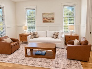 Un salon avec un canapé, deux fauteuils, une table basse et un tableau accroché au mur.