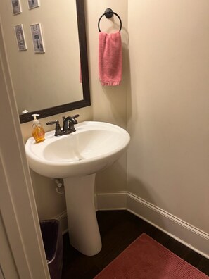 Ein Badezimmer mit einem weißen Waschbecken auf Säule, einem Spiegel, einem rosafarbenen Handtuch und einem Mülleimer.