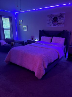 Ein Schlafzimmer mit einem Bett, einem Sessel, einem Nachttisch und einem Fenster.