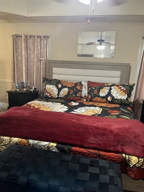 Een slaapkamer met een bed, een nachtkastje, een raam met zonwering en een plafondventilator.