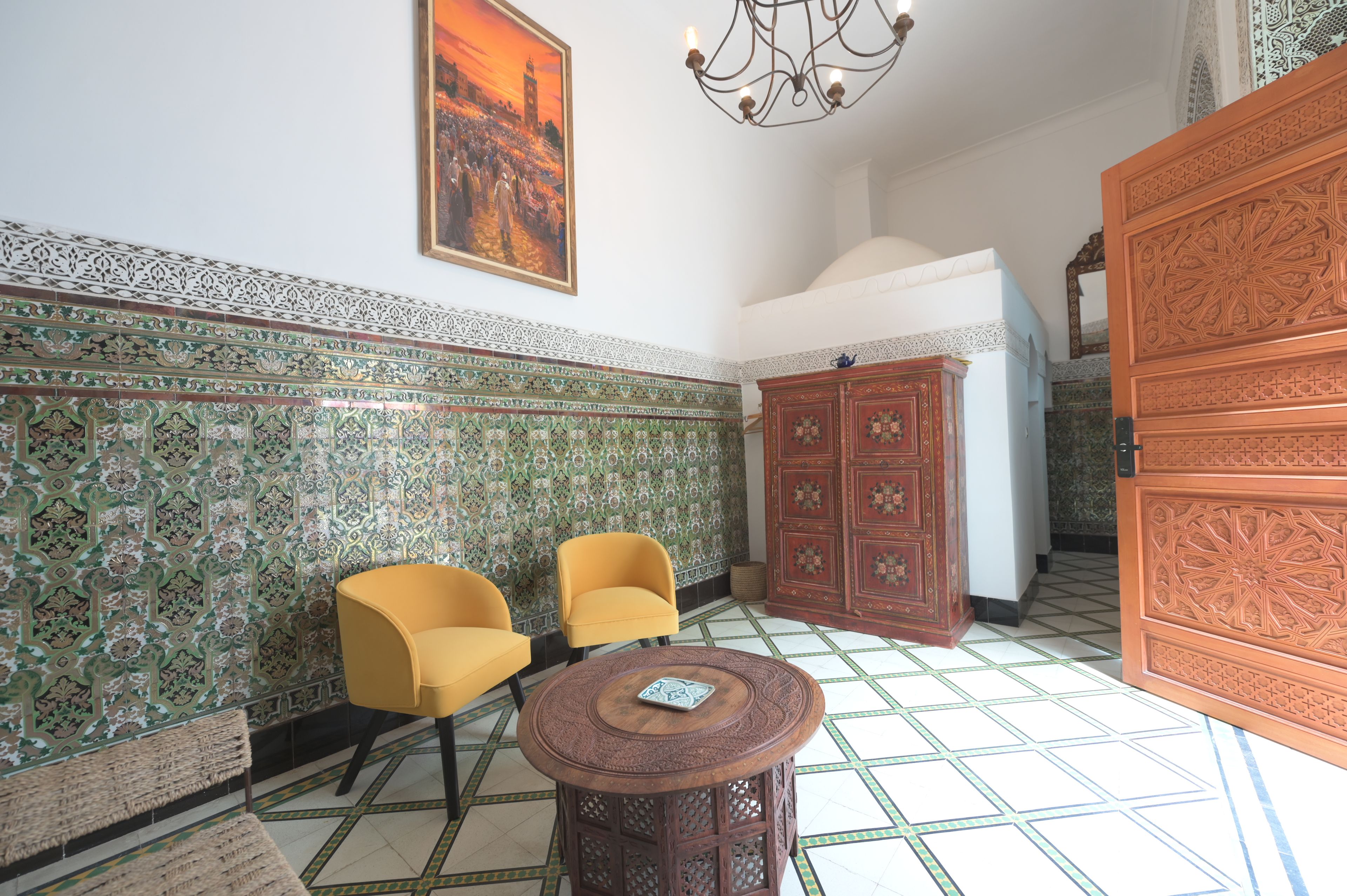 Une pièce aux murs ornés de motifs, avec deux chaises jaunes, une table en bois et un grand meuble.