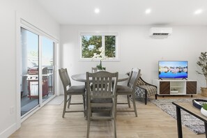 A modern living room with a dining area, a television, and a large window with a view of trees. - Carriage on Richter •2 King Beds• Sleeps 6 • Ski Base • Close to Hospital (Kelowna)
