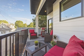 A balcony with a red chair, a wicker sofa, and a barbecue grill. - Carriage on Richter •2 King Beds• Sleeps 6 • Ski Base • Close to Hospital (Kelowna)