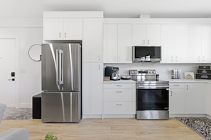 A modern kitchen with stainless steel appliances, white cabinetry, and a built-in microwave. - Carriage on Richter •2 King Beds• Sleeps 6 • Ski Base • Close to Hospital (Kelowna)