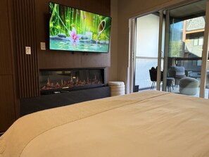 Une chambre d’hôtel équipée d’un lit, d’un téléviseur à écran plat fixé au mur, d’une cheminée et offrant une vue sur l’extérieur grâce à une porte-fenêtre coulissante.