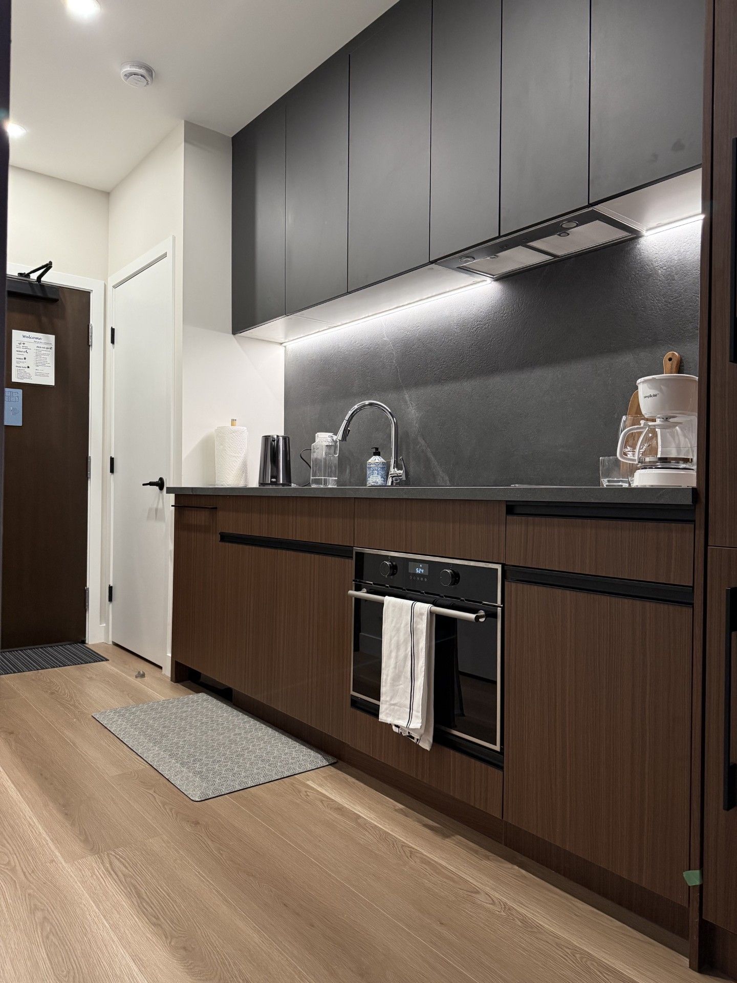 Una cocina moderna con armarios oscuros, un lavamanos de acero inoxidable y un horno empotrado.
