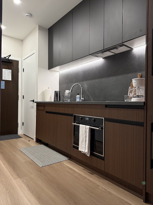 Una cocina moderna con armarios oscuros, un lavamanos de acero inoxidable y un horno empotrado.