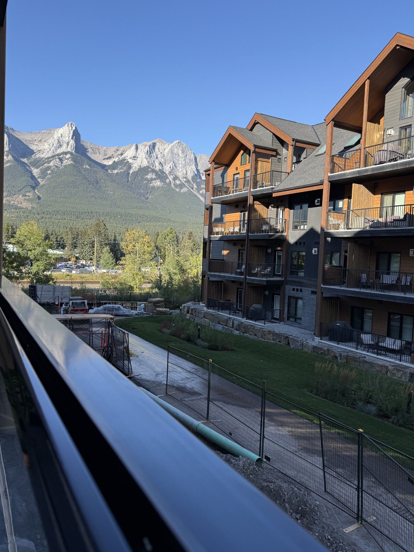 Un hotel de varios pisos con balcones, vistas a montañas y un área de estacionamiento.
