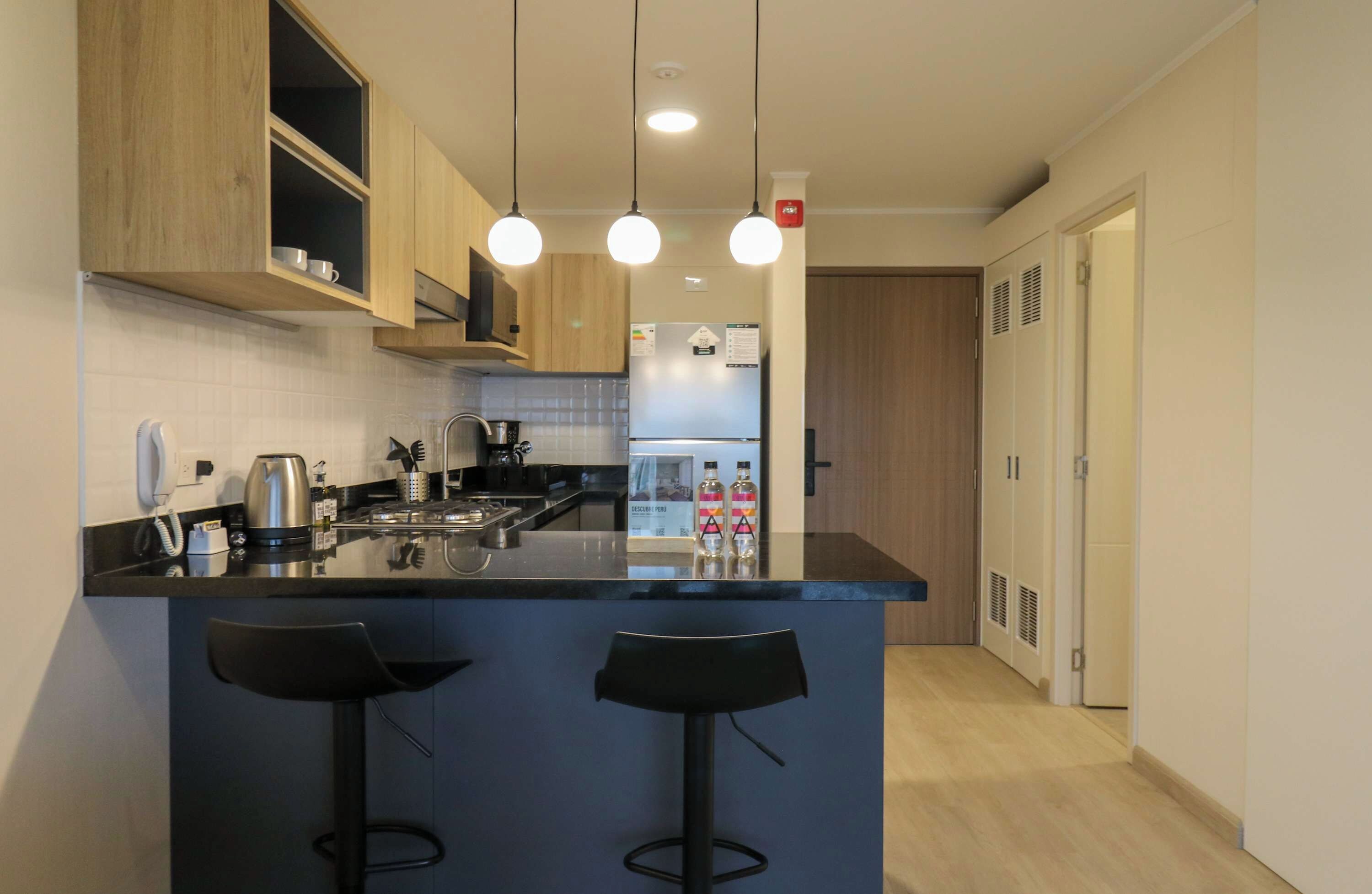 Una cocina moderna con una isla central, dos taburetes de bar, horno empotrado y refrigerador.