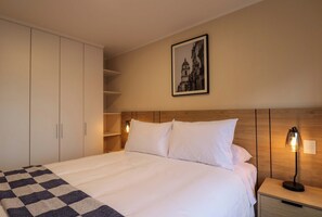 Una habitación de hotel con cama, mesita de noche, lámpara, armario y un cuadro en la pared.