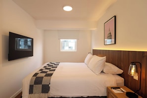 A hotel room with a bed, a bedside table with a lamp, a framed picture on the wall, and a window. - w* | Amazing 2BR w/ Partial Sea View in Miraflores (Miraflores)