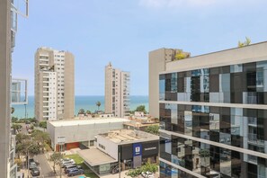 A modern building with a glass facade, a visible store named 'TRAMONTINA,' and a view of the sea in the background. - w* | Amazing 2BR w/ Partial Sea View in Miraflores (Miraflores)