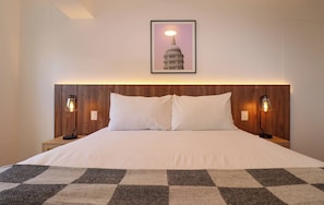 A hotel room with a large bed, two bedside lamps, a framed picture of a building, and a checkered throw on the bed. - w* | Amazing 2BR w/ Partial Sea View in Miraflores (Miraflores)
