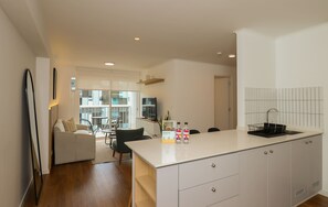 A modern kitchen with a central island, a dining area with a sofa and chairs, and a view of a balcony. - w* | Amazing 2BR w/ Partial Sea View in Miraflores (Miraflores)