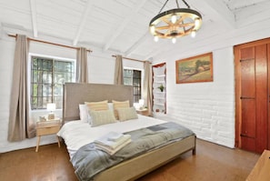 A bedroom with a large bed, a wooden headboard, a hanging light fixture, and a window with curtains. - Rustic Urban Homestay • Pet-friendly (Pomona)